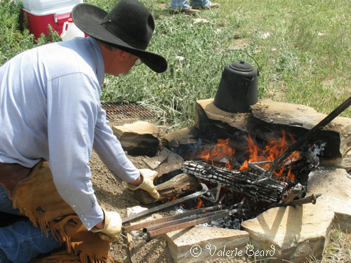 ©Valerie Beard, Short Grass Studios photo of a cowbow tending a fire encased in a rock circle where branding irons and a coffee pot are heating up