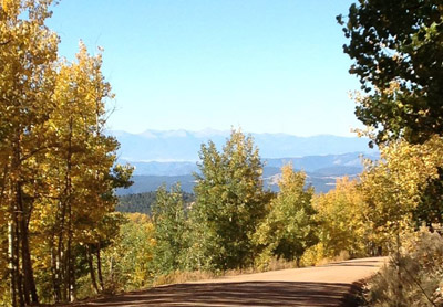 © S.L.Reay photo of a dirt road with a view of a valley and mountains in the distance and aspen trees in the foreground turning gold